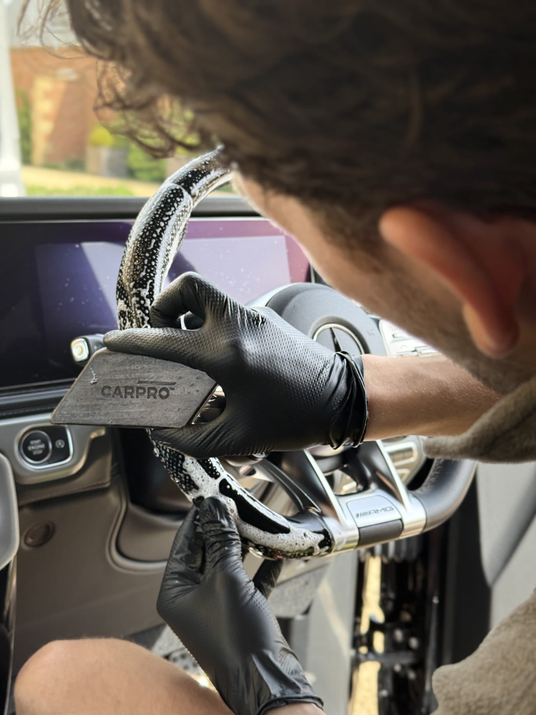 Detailer coating the steering wheel trim of a Mercedes with a CarPro applicator