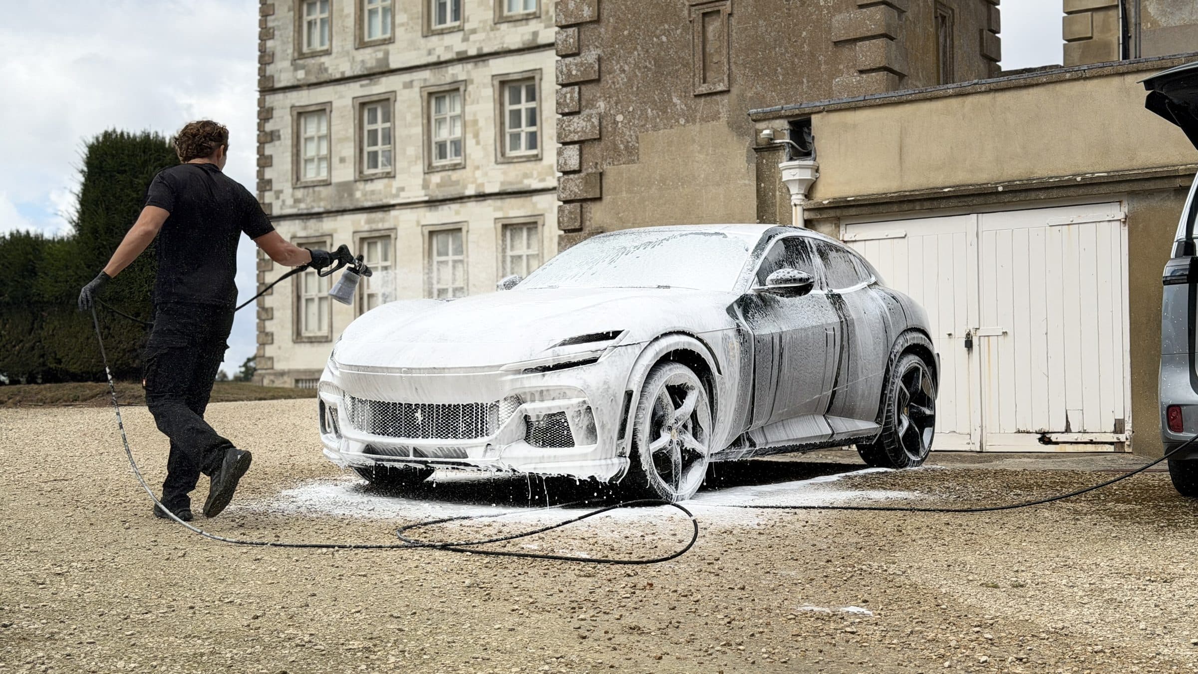 Detailer snow foaming a Ferrari Purosangue outside a stone country house