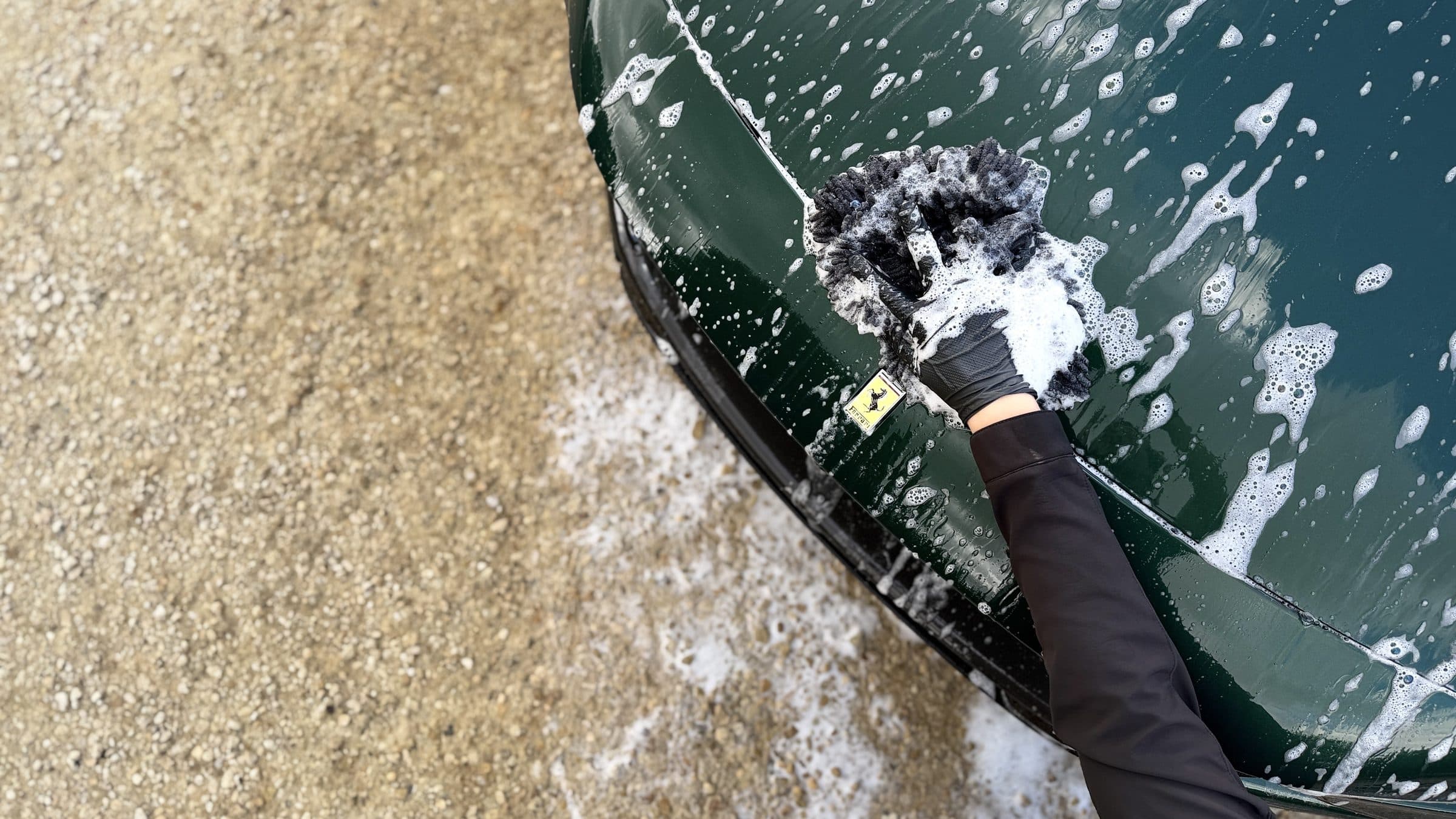 Wash mitt working foam across the wing of a dark green Ferrari