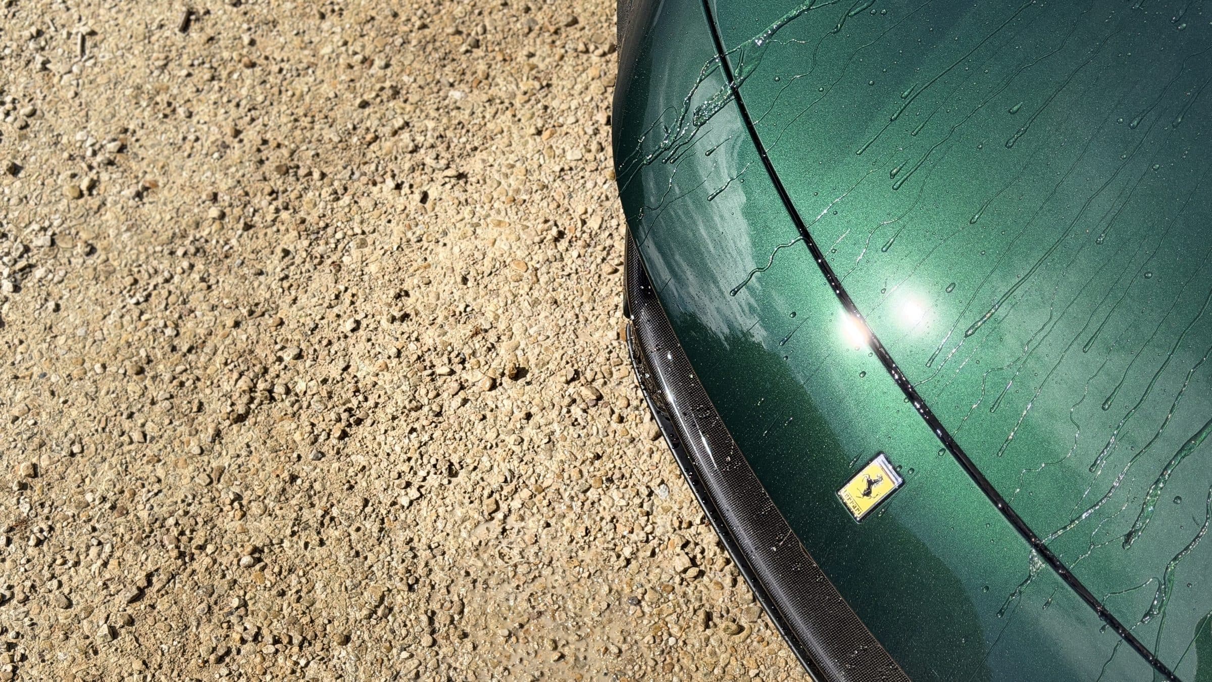 Water beading on the bonnet of a dark green Ferrari beside a gravel drive