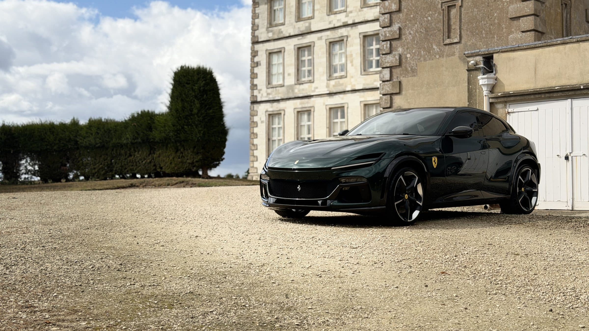 Dark green Ferrari Purosangue on the gravel drive of a stone country house
