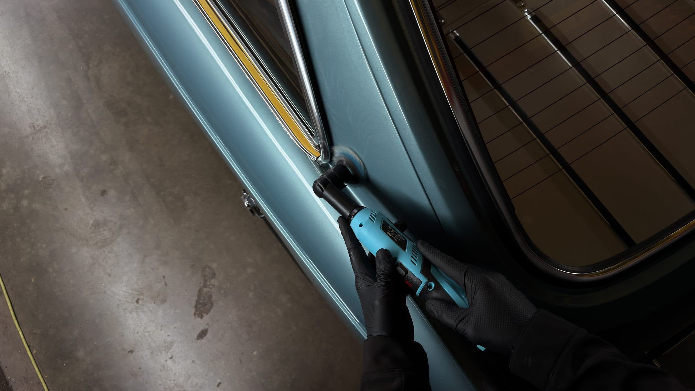 Gloved hands machine polishing the window frame of a light blue MGB GT
