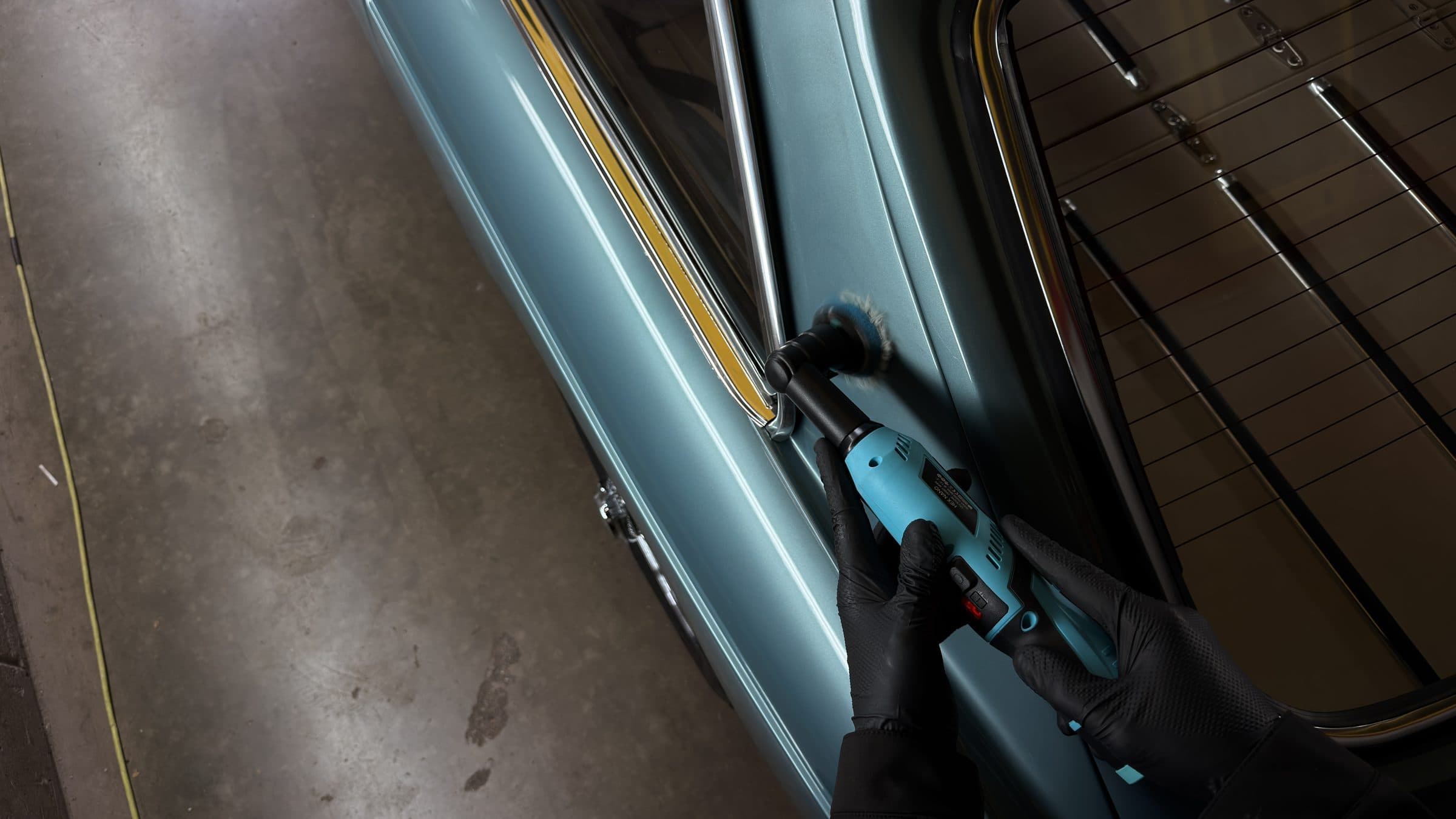 Compact polisher working along the window frame of a light blue MGB GT