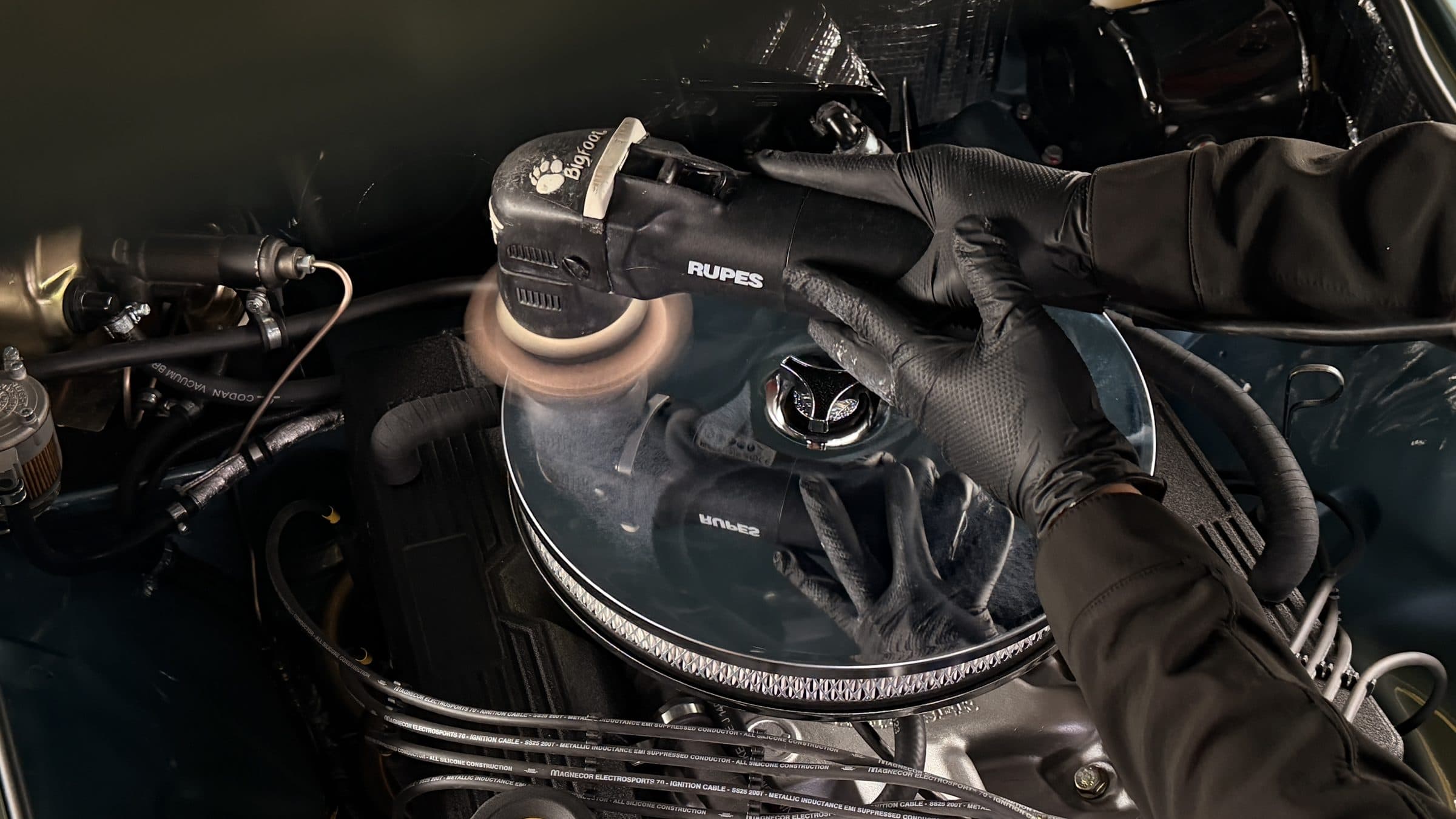 Machine polisher refining the air filter cover in a classic car's engine bay