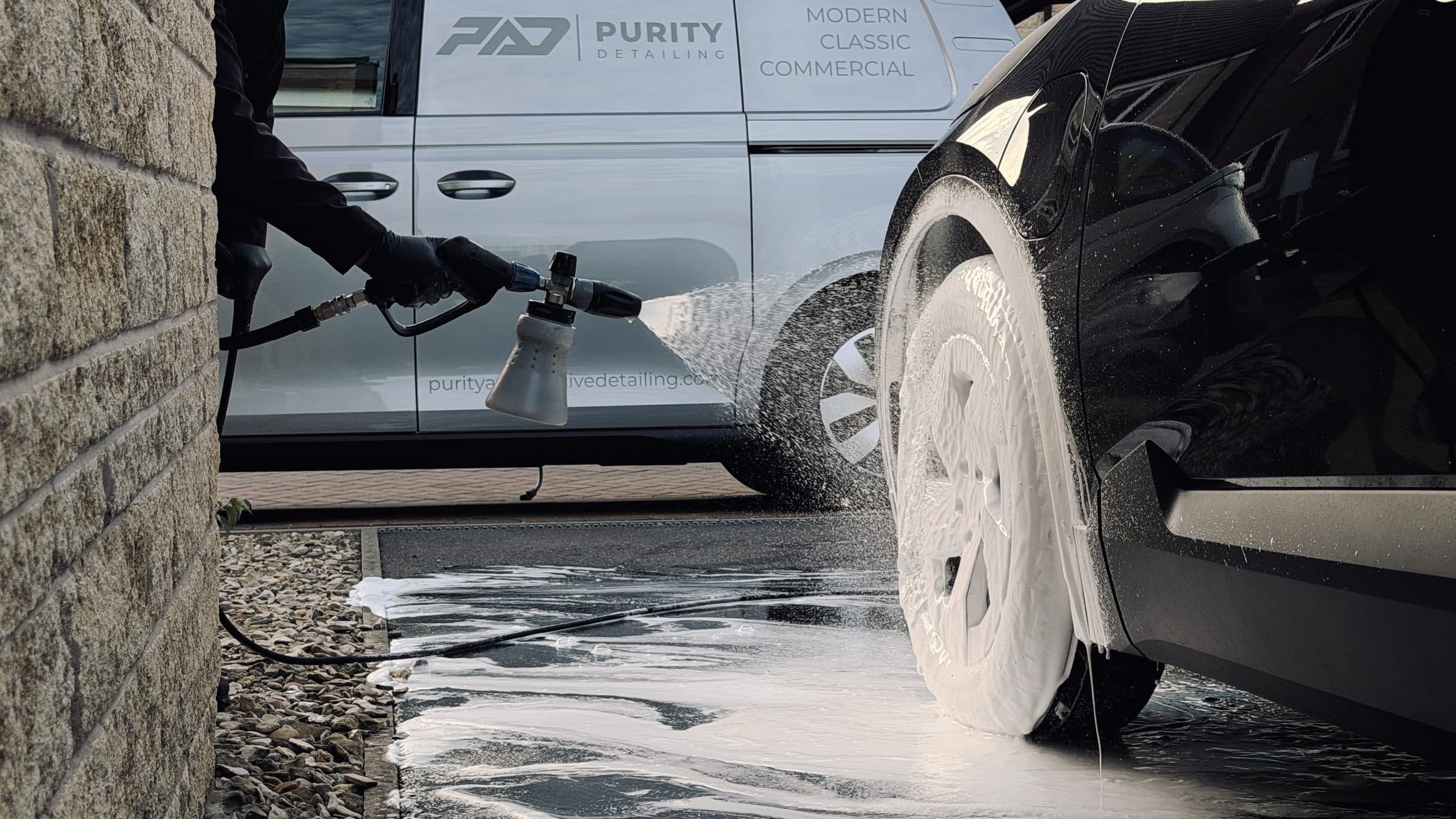 Snow foam rinse on a black car's wheel beside the Purity Detailing van