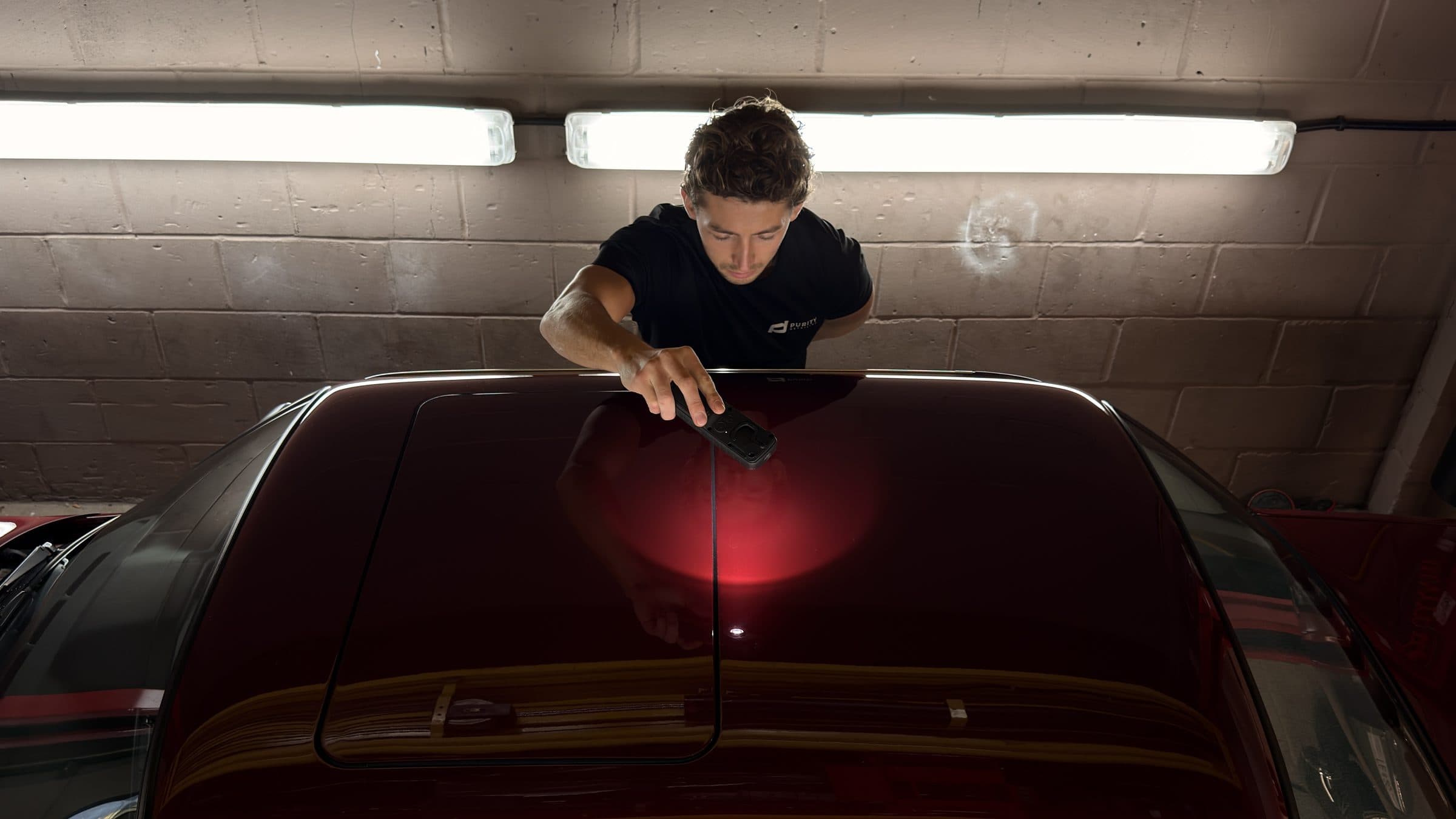 Detailer checking the dark red roof of a car with a handheld inspection light