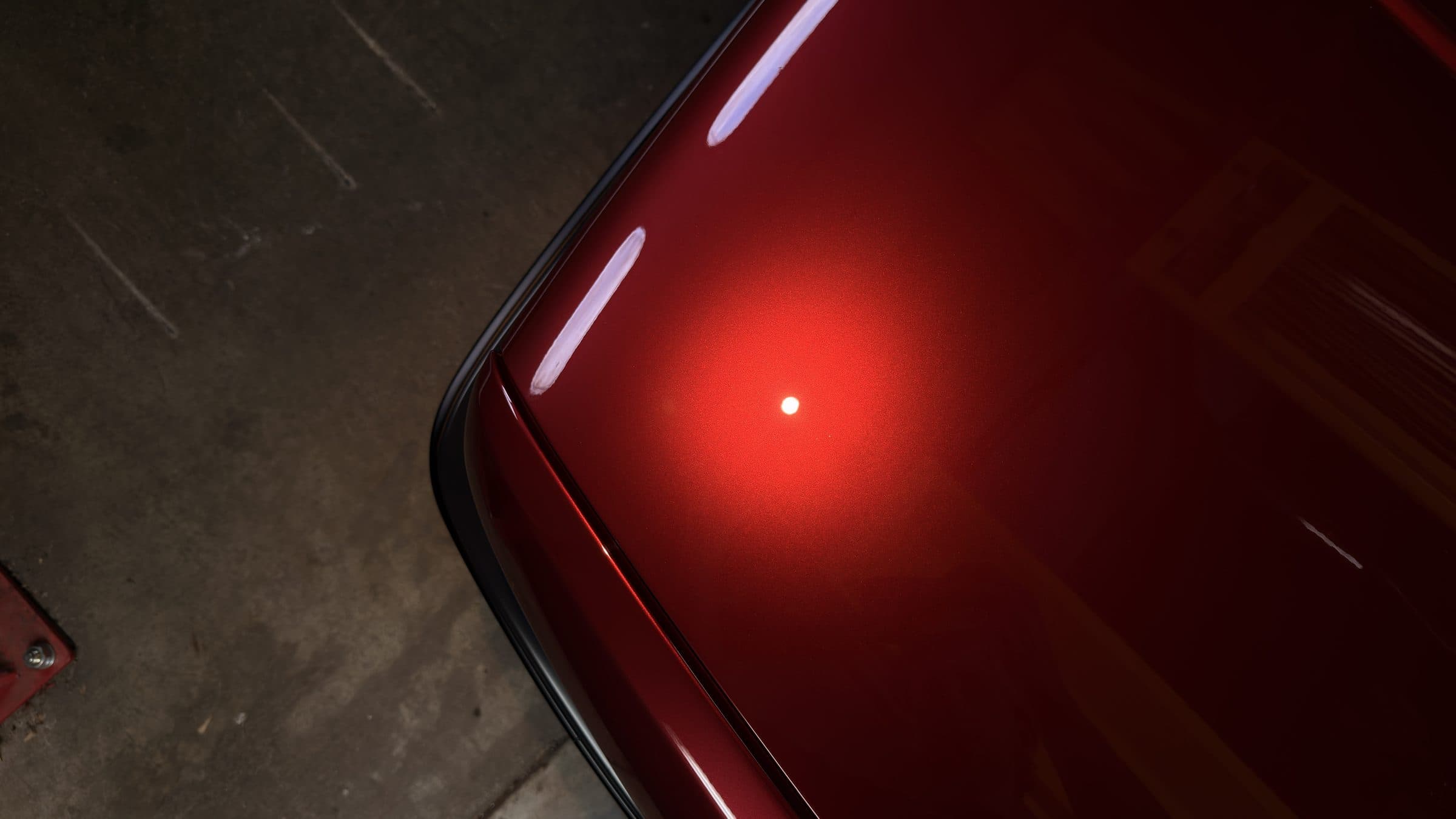Inspection light reflected in dark red metallic paint at the corner of a car panel